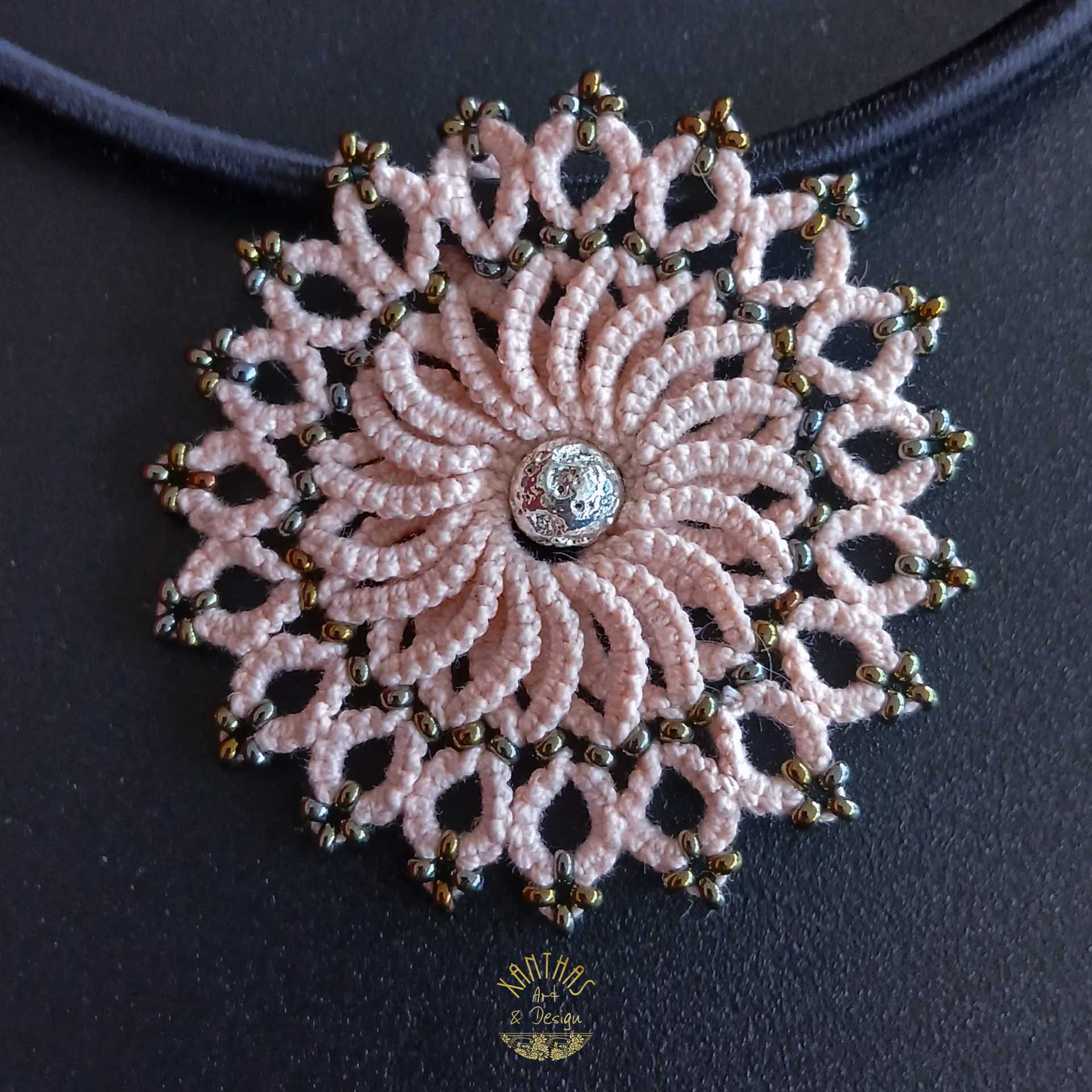 Collier „Clio“ aus handgefertigter Frivolitätenspitze in Zartrosa/Lachs mit rundem Anhänger, silber galvanisierter Lavaperle in der Mitte und bronzefarbigen Rocailles. Die schwarze Textilhalskette hat einen silberfarbenen Verschluss mit Verlängerungskette.