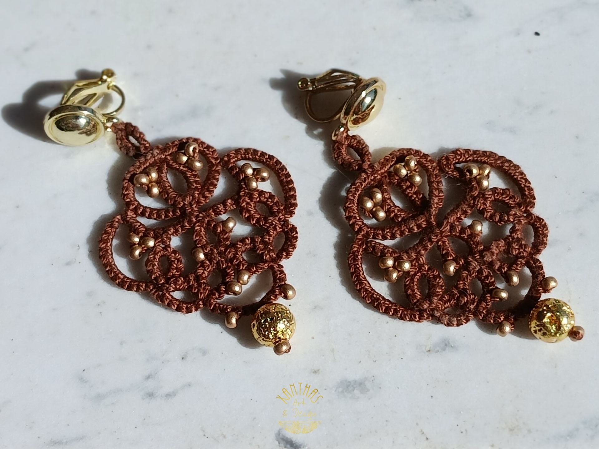 Ohrclips „Amandine“ aus handgefertigter Frivolitätenspitze in Dunkelbraun mit gold bedampften Rocailles und gold galvanisierten Lavaperlen. Die Ohrclipspatente sind aus goldfarbigem Metall.