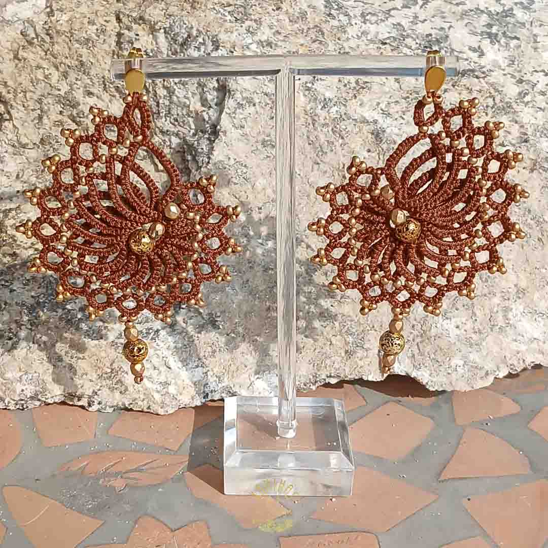 Handgefertigte Ohrringe in dunkelbraun mit goldenen Perlen und Edelstahl-Ohrsteckern. Geknüpft aus Baumwollgarn und mit goldenen Akzenten verziert.
